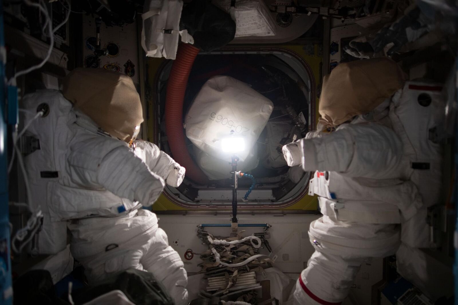 Astronautas ao lado de um traje espacial dentro da Estação Espacial